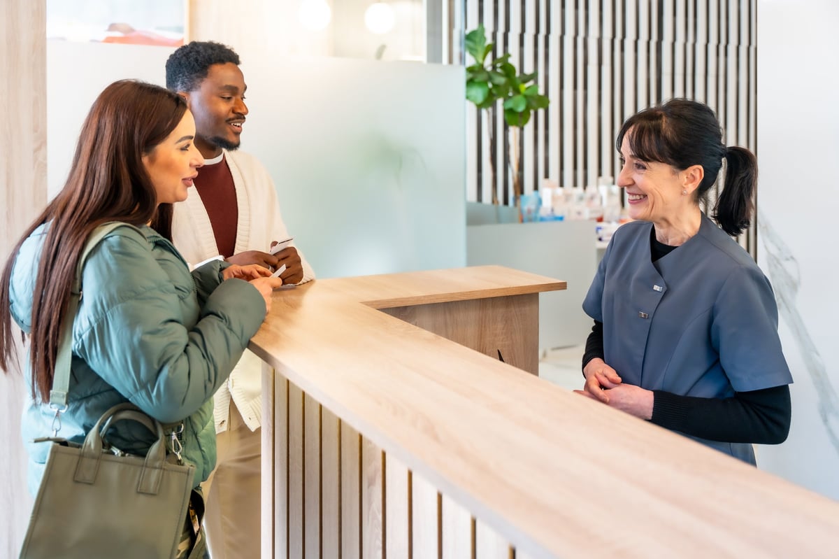 Patients discussing appointment details with a receptionist at a modern dental clinic